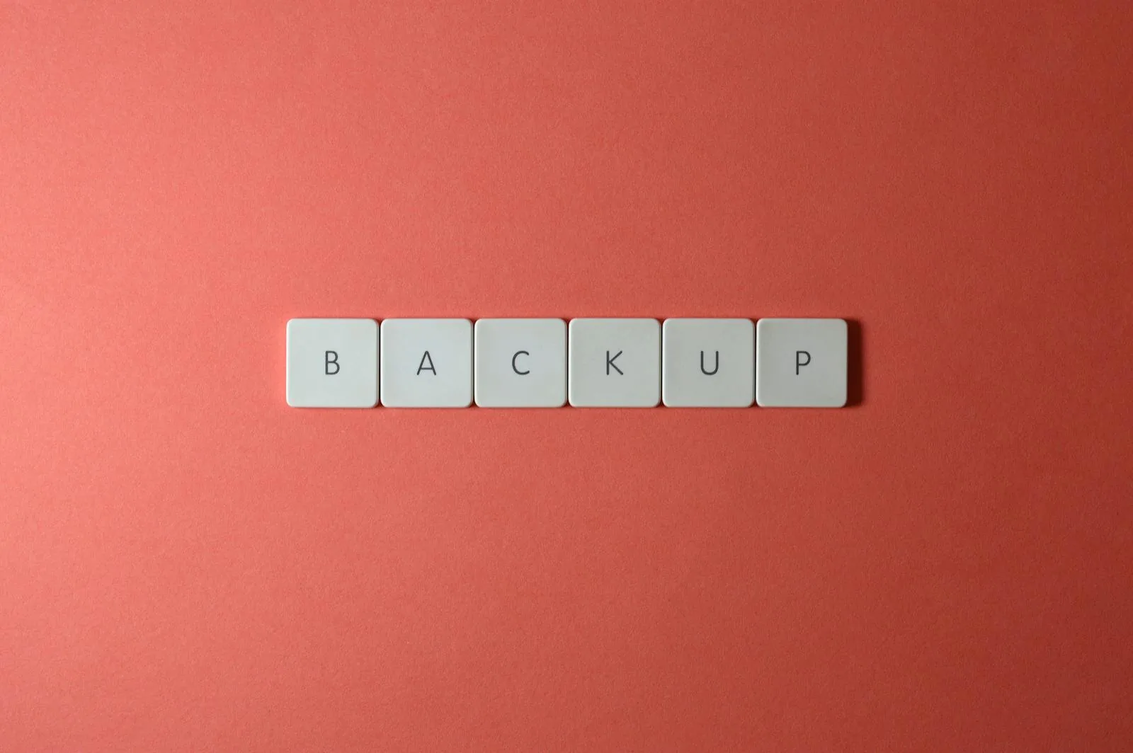 Các phím bàn phím màu trắng ghép thành chữ BACKUP trên nền đỏ san hô, nhấn mạnh tầm quan trọng của sao lưu seed phrase crypto