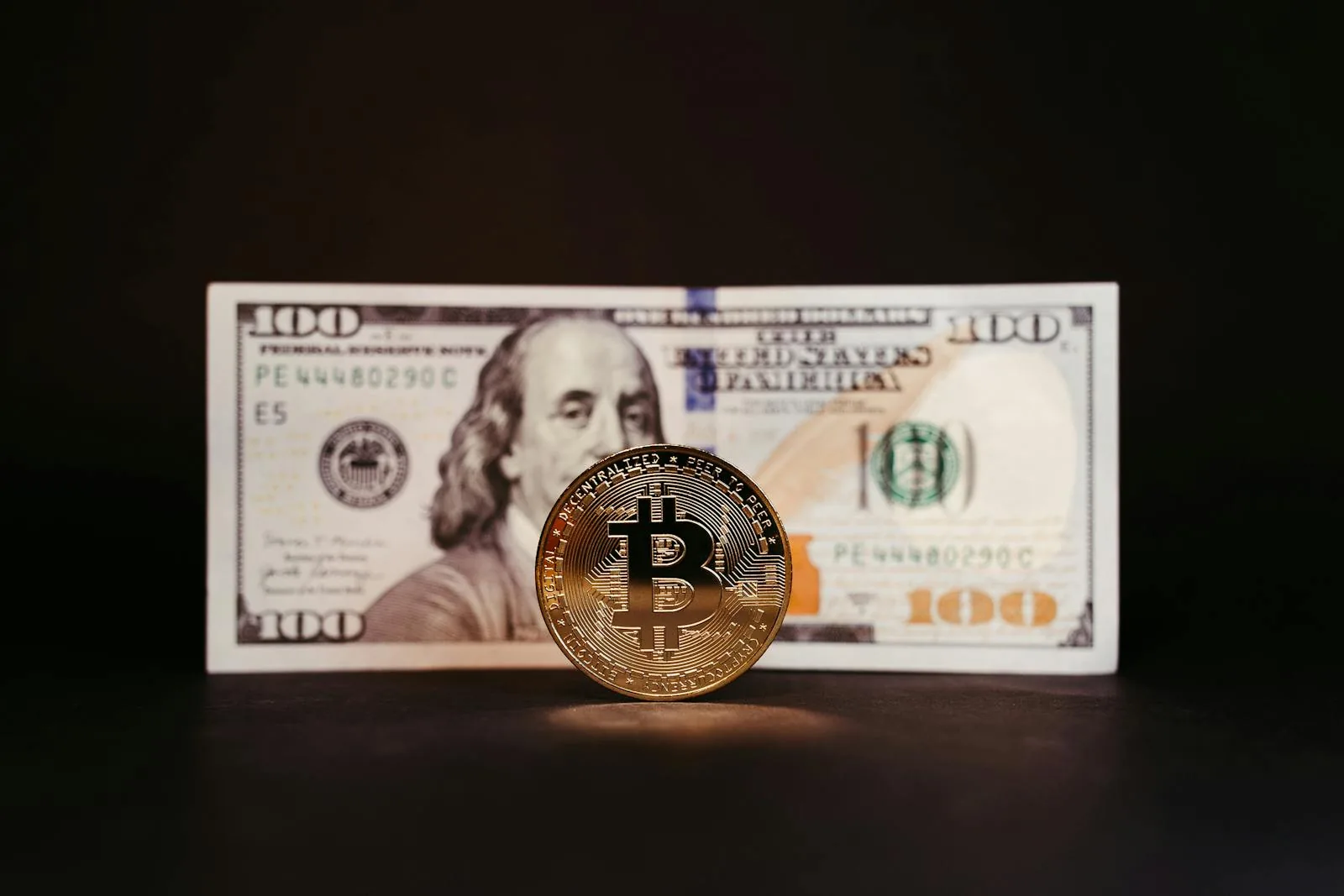 Đồng coin Bitcoin vàng đặt trước tờ tiền 100 USD, tượng trưng cho stablecoin USD-backed